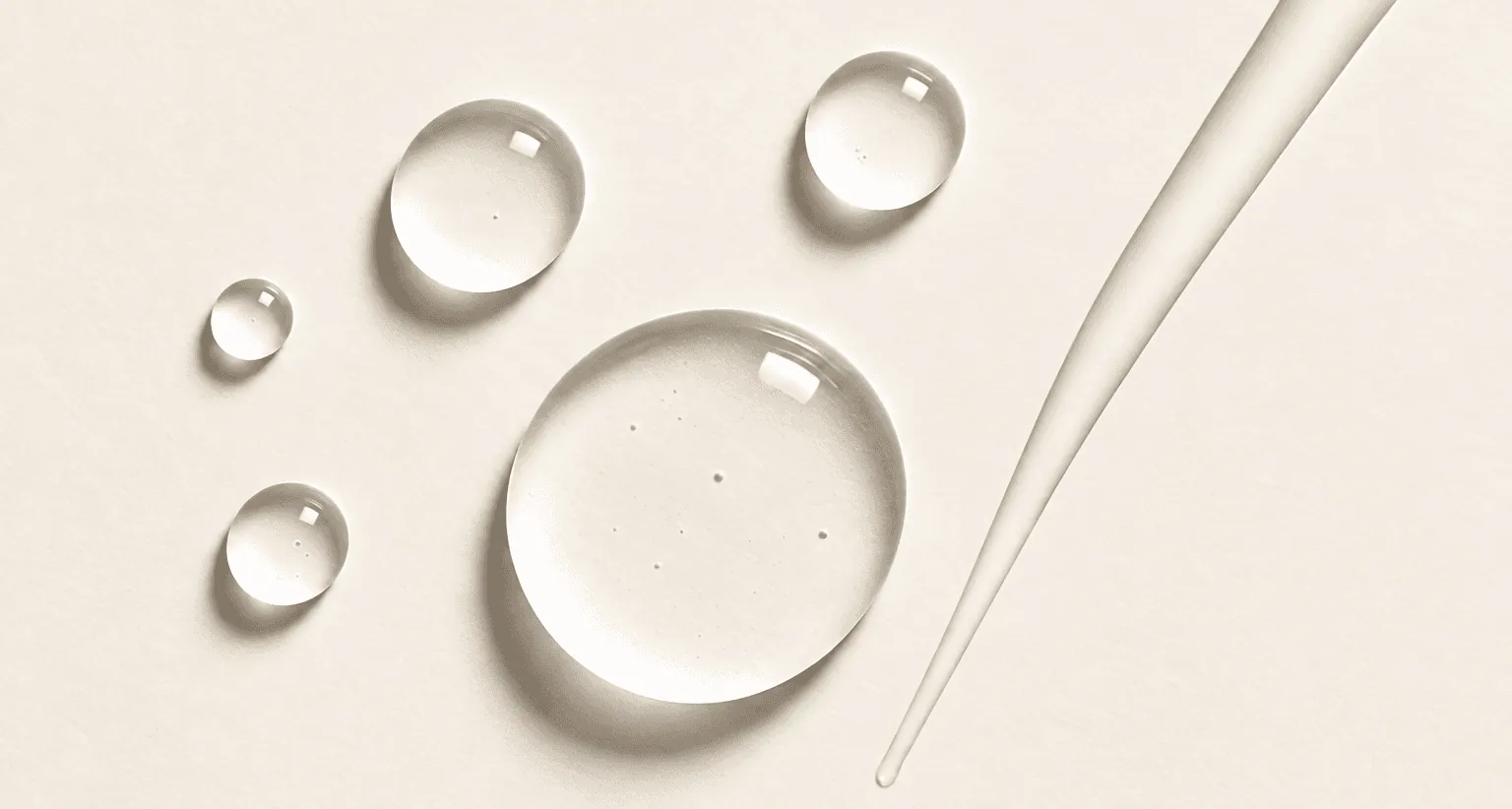 Clear skincare droplets and a glass applicator on a neutral surface